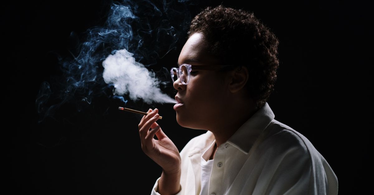 Close-up of a woman in glasses exhaling smoke against a dark background.